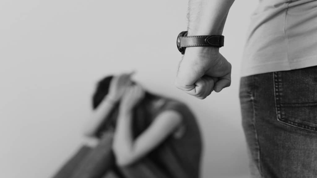 Man Clenching Fist Near a Woman Covering Face While Sitting