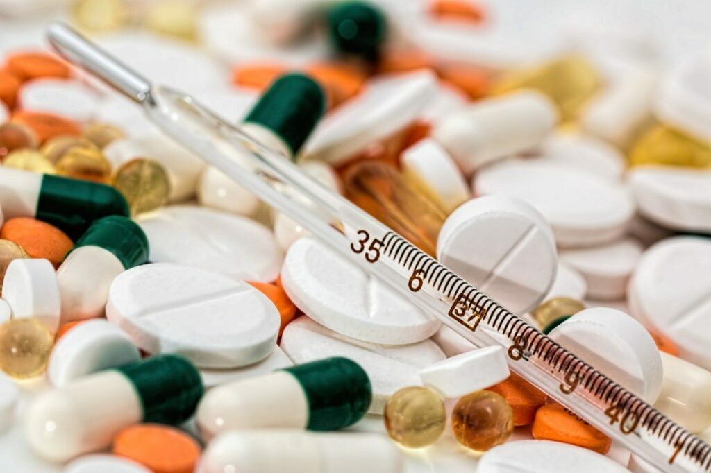 A transparent thermometer lying on the multicolor medicine pills.